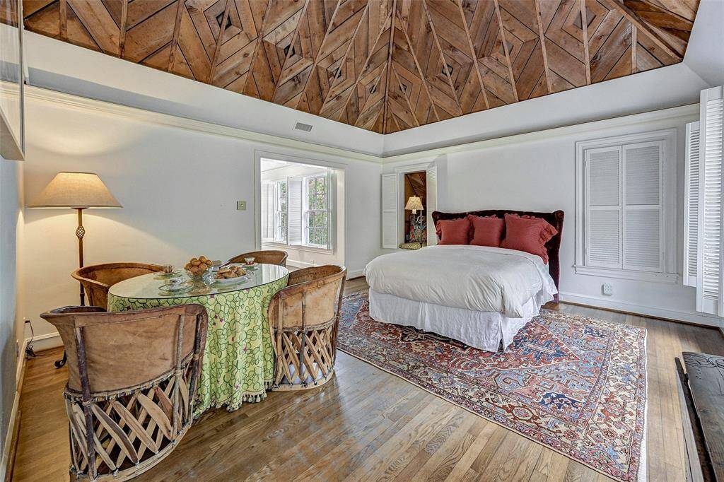 Privately tucked away, The spacious primary suite is full of natural light, original hardwood floors and a custom vaulted ceiling with rustic beams