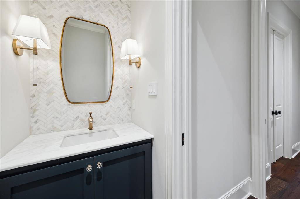 Herringbone backsplashes, brass accents, light and clean white trim and dark cabinets define this handsomely designed guest bathroom.