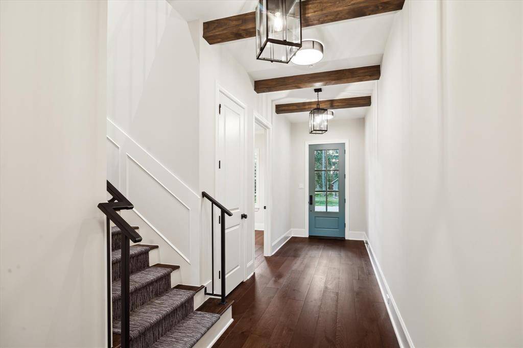 Gorgeous dark wood beams and hardwood floors accent the light bright walls and white trim in the entry with tall ceilings and custom lights.