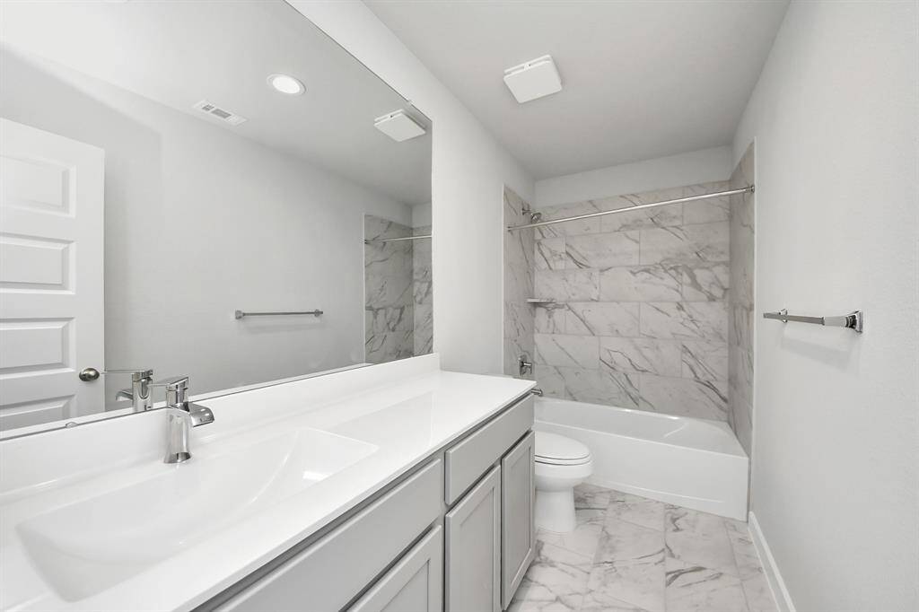 Secondary bath features tile flooring, bath/shower combo with tile surround, light stained wood cabinets, beautiful light countertop. Sample photo of completed home with similar floor plan. Actual colors and selections may vary.