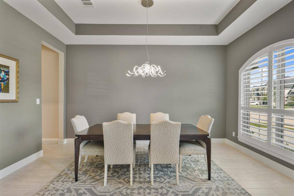Formal dining room elegantly framed by a tiered ceiling, wooden shutters, and a stunning custom chandelier.