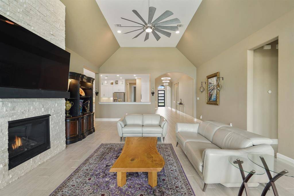 This spacious living area features a vaulted ceiling and a remote-operated gas fireplace with a striking stone surround, offering an open view to the kitchen and entryway — creating the perfect setting for entertaining.