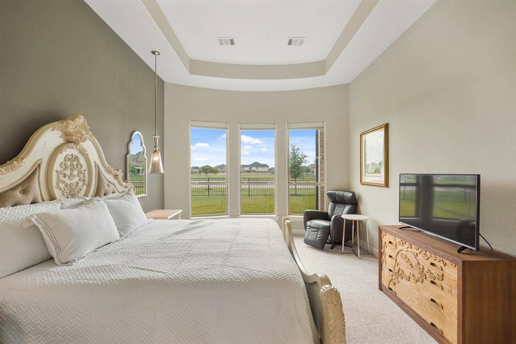 Another view of the primary bedroom featuring a tray ceiling and large bay windows, filling the space with natural light, and providing a peaceful view of the lake.