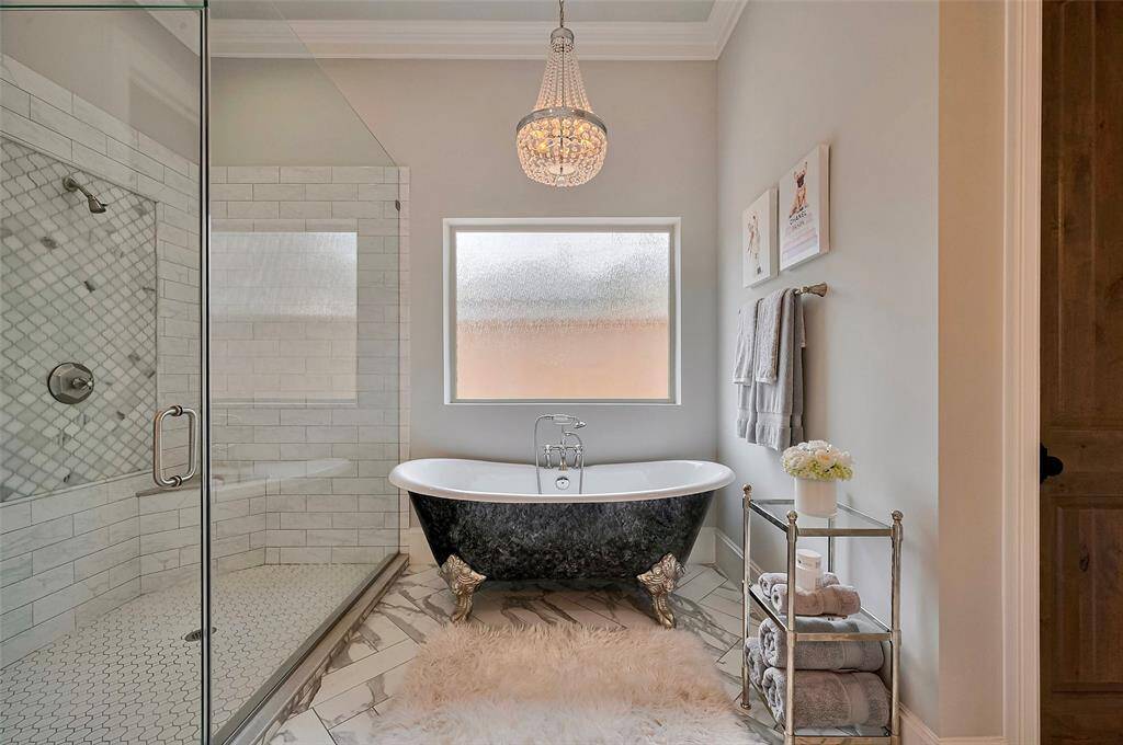 Indulge in the spacious shower and unwind in the oversized claw foot iron tub, the centerpiece of this serene retreat. A crystal chandelier adds a touch of glamour, casting a soft glow that enhances the spa-like atmosphere of this thoughtfully designed primary bath.
