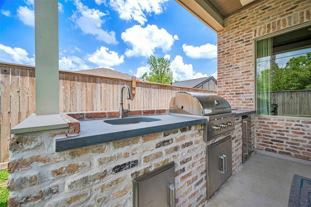 The brick-enclosed outdoor kitchen is fully equipped with a built-in gas grill, refrigerator, ample counter space, sink, and generous storage—an ideal setup for effortless entertaining and elevated al fresco dining.