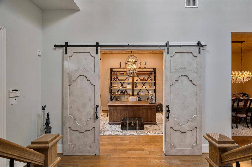 Step into a thoughtfully curated home office where sophistication meets charm. Framed by custom-designed barn doors, this stylish study offers both privacy and presence. A vintage birdcage chandelier adds a touch of timeless elegance, casting a warm glow over the space. Positioned with a picturesque view of the front of the home, natural light pours in, creating an inspiring environment for productivity or quiet reflection. It’s a perfect blend of form and function—where design details elevate the everyday.