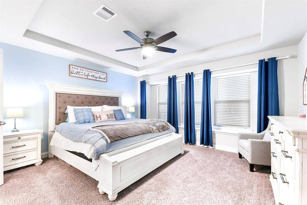 Primary bedroom featuring a stylish tray ceiling, a ceiling fan for added comfort, and a cozy sitting area by the windows.