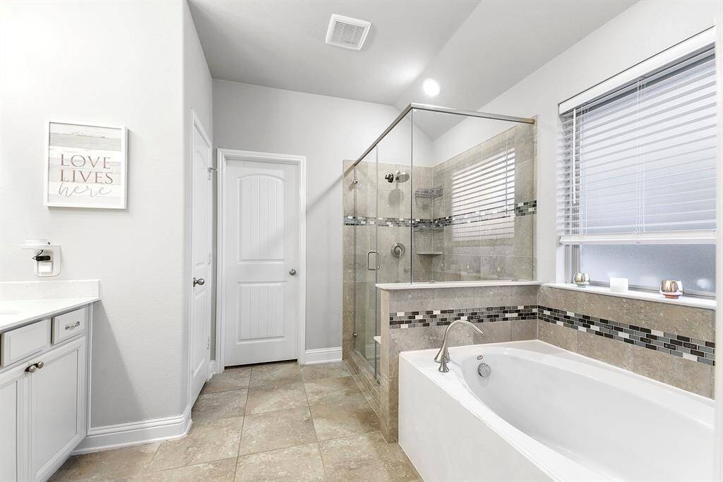 Luxurious primary bath featuring a separate shower and relaxing soaking tub, dual vanities with elegant white granite countertops, and sleek white cabinets enhanced with hardware.