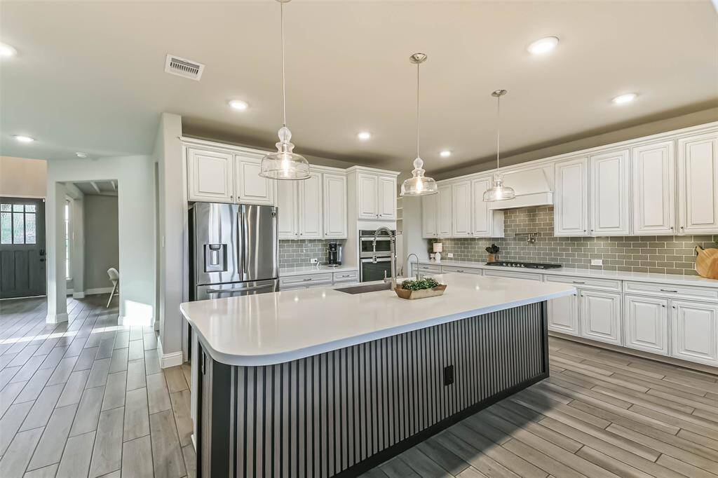 The island with its custom wood wrap is another custom touch in this beautiful home. Quartz counters galore, breakfast bar, pendant lights, subway tile backsplash, specialty cabinets, gas cooktop, and pot filler add beauty and functionality to this spacious kitchen.