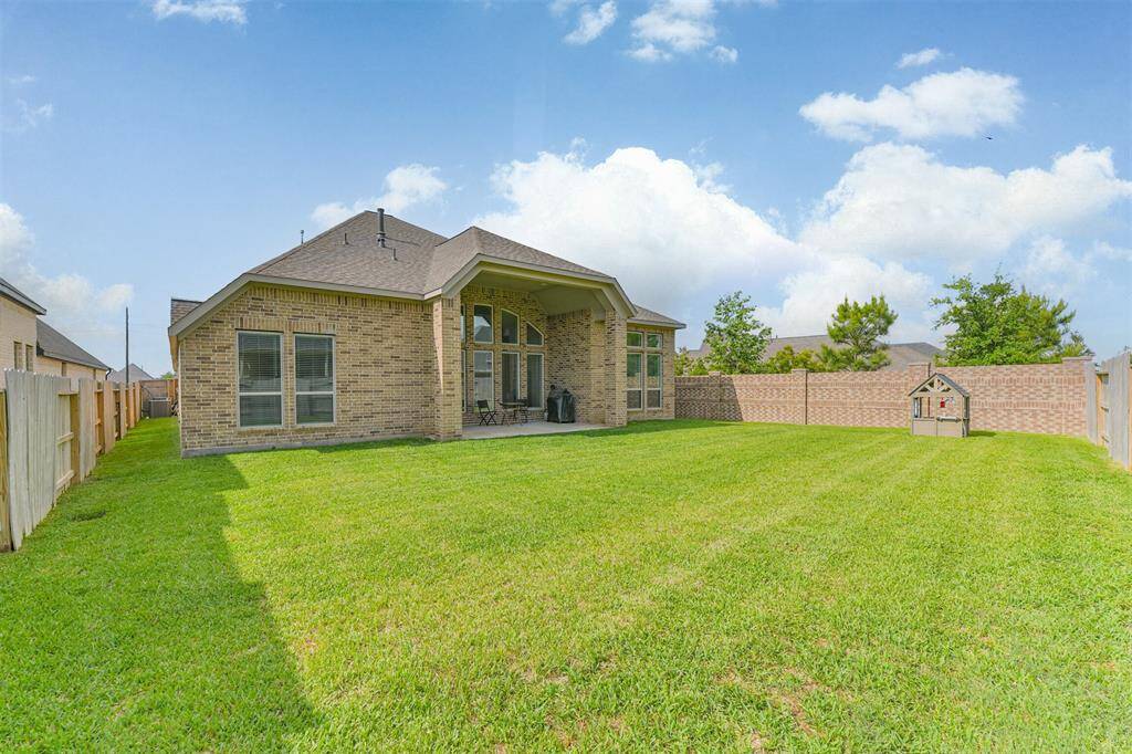 One side of backyard has brick fence and trees adjacent to it - next to a playground