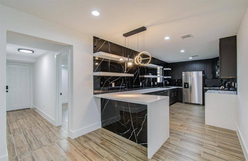 This is a modern kitchen with a sleek, sophisticated design. It features dark cabinetry with clean lines, contrasted by a striking tiled Carrara marble backsplash w/white veining, adding a touch of luxury to the space.