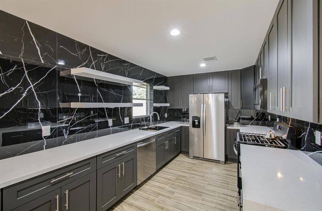 The countertops are bright white, providing a refreshing contrast to the dark tones of the cabinets and backsplash.The kitchen island extends outward, creating a spacious surface for dining or entertaining.