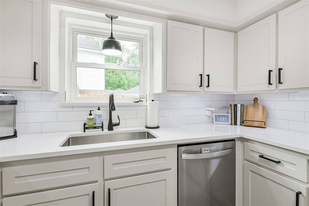 A large stainless steel basin sink with a quaint window elevating the light and airy feeling in the kitchen.
