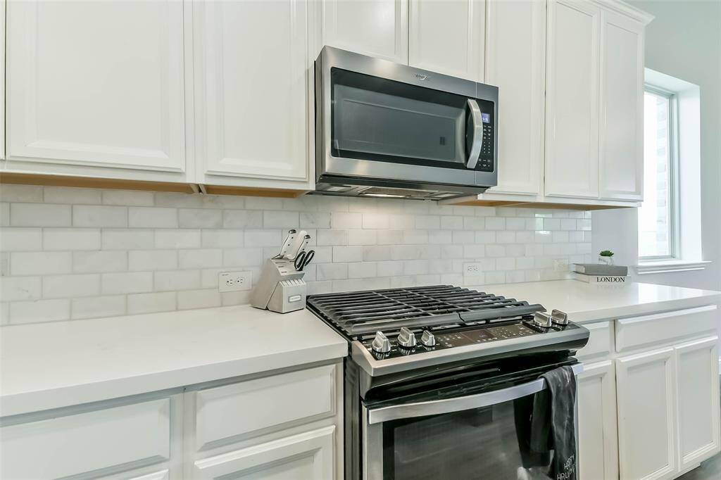 Upgraded subway tile backsplash highlights the beautiful quartz counters and gas range.