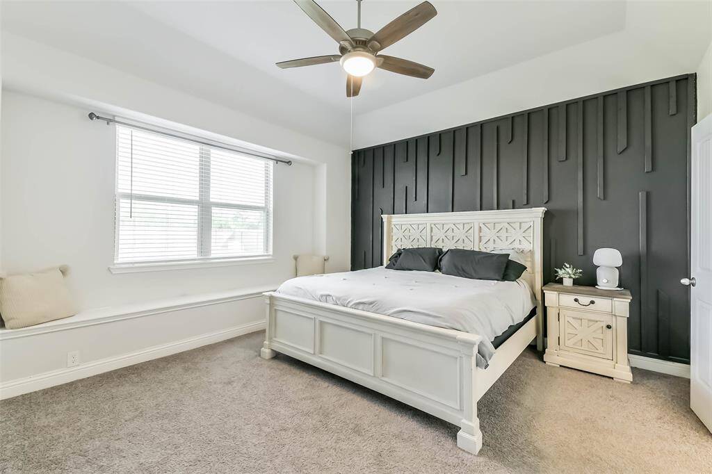 Another accent wall enhances the look of this primary bedroom with its ceiling fan and window seat.