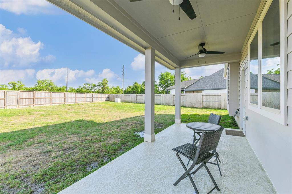 Extended covered back porch with gas stub and ceiling fans looks towards woods on the other side of the fence.