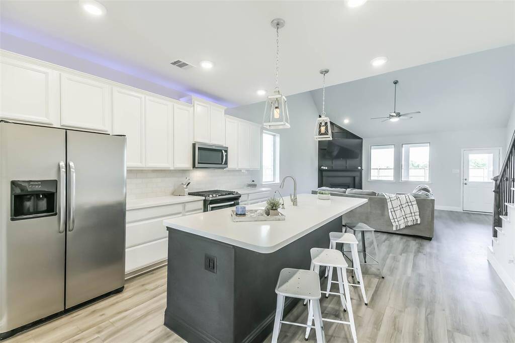 Beautiful kitchen carries on the black and white theme with black extended island and breakfast bar, white cabinets, quartz countertops, pendant lighting, and uplighting above the cabinets.