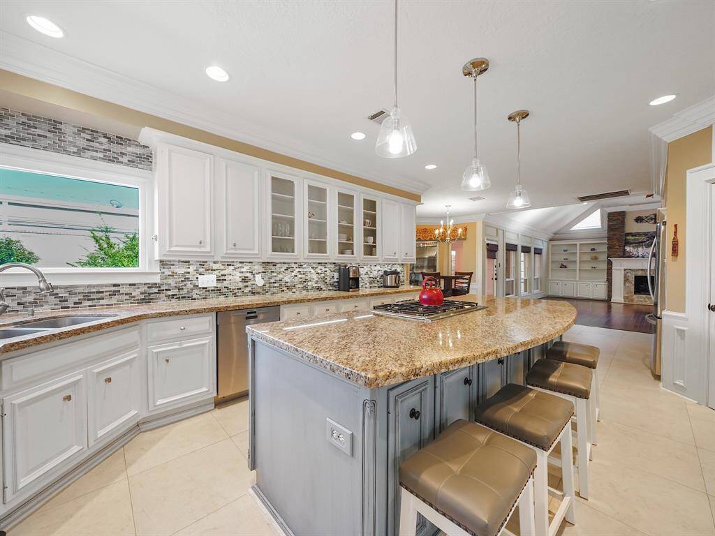 The oversized island in a soft blue-gray hue, perfectly designed to enhance both functionality and style. This inviting centerpiece offers ample additional seating, making it ideal for entertaining guests or enjoying casual family meals. The island beautifully contrasts with the pristine white cabinetry and elegant glass tile backsplash, creating a harmonious blend of colors that elevates the overall aesthetic of the kitchen.