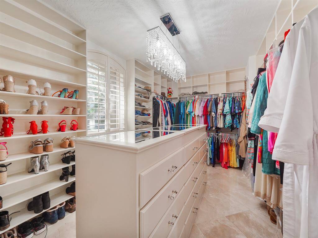Step into luxury with this stunning custom-designed walk-in closet, meticulously crafted to elevate your organization and style. Featuring ample storage solutions, this spacious retreat is adorned with elegant chandelier lighting that adds a touch of sophistication. The built-in dresser offers convenience and functionality, while a charming window with plantation shutters allows natural light to filter in, creating a warm and inviting atmosphere.