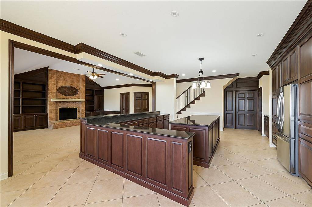 The chef’s kitchen blends seamlessly with the living room, offering dark wood cabinetry, granite counters, and an oversized island. A brick fireplace anchors the space with rustic warmth.