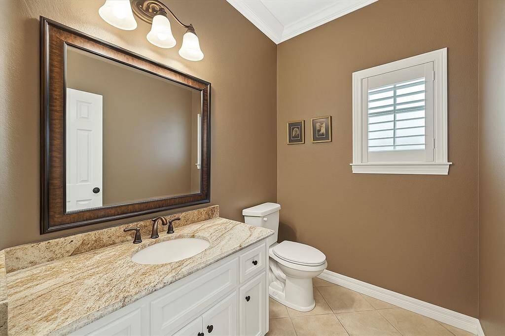 The powder room combines luxury and comfort with a granite vanity, rich-toned walls, and classic molding. A framed mirror and bronze fixtures elevate the look for guests and everyday use.