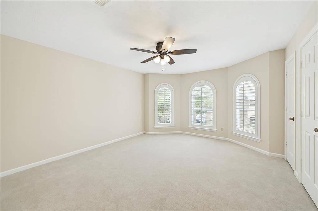 This bright and airy primary bedroom features three elegant arched windows with plantation shutters, allowing for soft natural light and added privacy. Neutral tones and plush carpet create a peaceful setting.