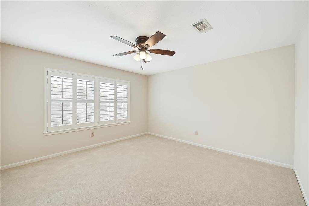 Sunlight streams through charming arched windows in this inviting secondary bedroom, complete with neutral tones, soft carpeting, and a ceiling fan for year-round comfort. Shutters add timeless appeal while ensuring privacy in this peaceful and versatile space.