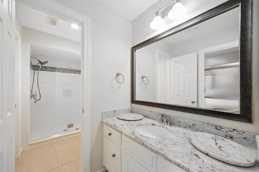 A second full bathroom shines with modern finishes, including a granite countertop, sleek white vanity, and a spacious glass-enclosed shower with custom tile detail. Elegant lighting and a wide framed mirror add a polished, contemporary feel to this stylish space.