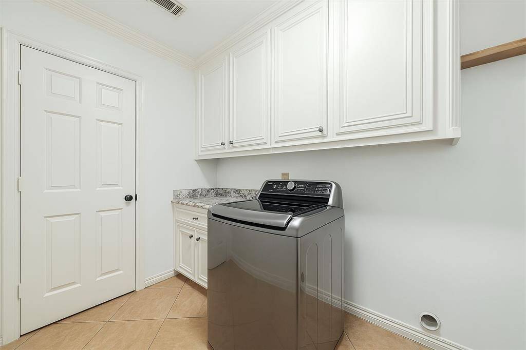 Efficiency meets elegance in this well-designed laundry room featuring a granite countertop for folding, ample cabinetry for storage, and a modern top-load washer. Thoughtfully laid out for convenience, it combines function with clean, classic style in every detail.