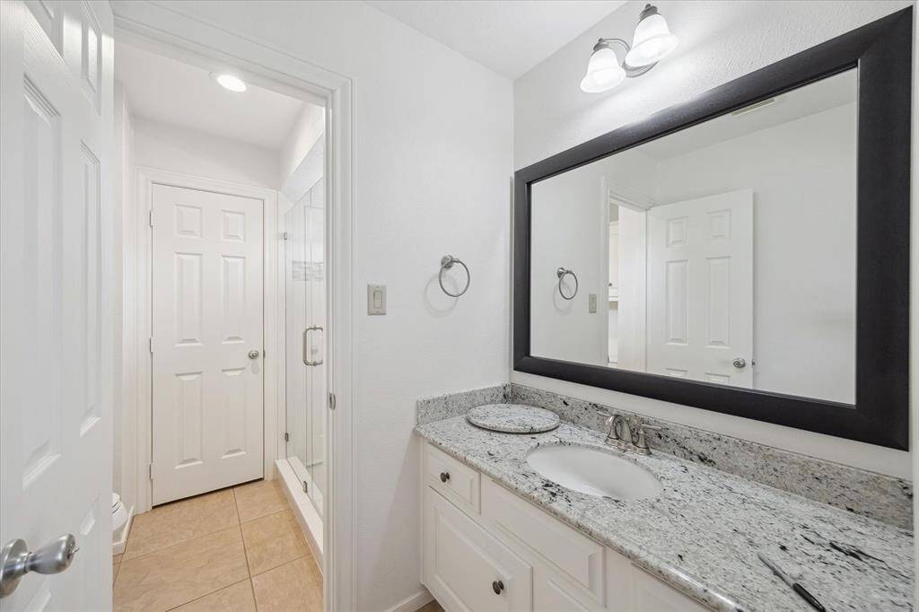 This beautifully updated bathroom boasts a clean, modern aesthetic with crisp white cabinetry, a stunning granite countertop, and a large framed mirror. The sleek tile flooring and glass-enclosed shower create a spa-like retreat—perfect for starting or ending your day in comfort and style.