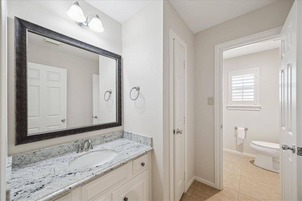 A stylish and functional powder room boasting granite countertops, elegant cabinetry, and a framed mirror. With separate water closet access, it provides added privacy and efficiency in a crisp, neutral palette perfect for guests and daily use.