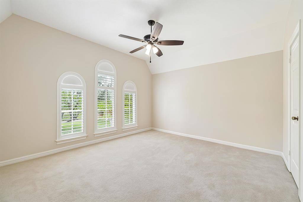 A serene retreat awaits in this spacious bedroom featuring soaring vaulted ceilings and a trio of arched windows with shutters. Natural light floods the space, highlighting the soft neutral palette and plush carpeting – a perfect blank canvas for your dream bedroom.