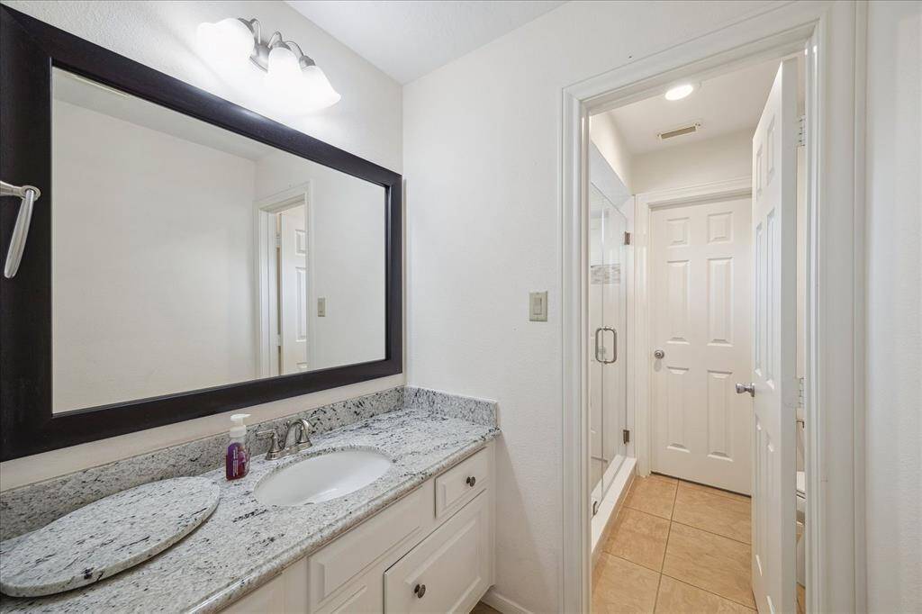 Featuring granite counters, white cabinetry, and a generous mirror, this bathroom is both practical and polished. The adjoining walk-in shower, with its modern tile detailing and glass doors, offers a spa-like touch to your daily routine.