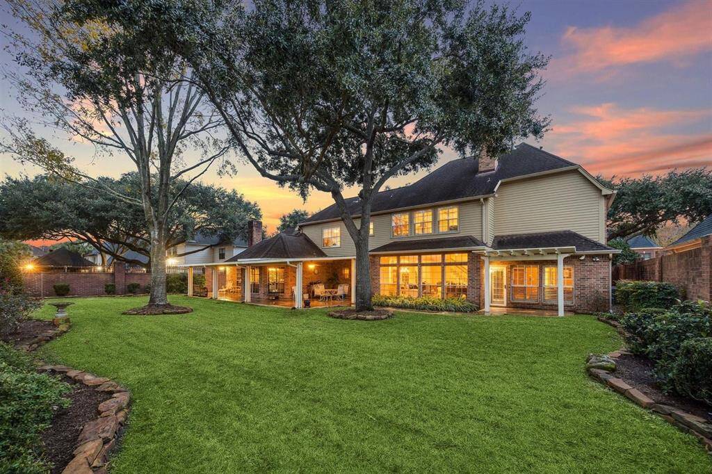 Bask in the beauty of this expansive backyard oasis at sunset, where mature shade trees and lush landscaping frame the perfect space for gatherings or tranquil moments. The covered patio invites you to relax and unwind beneath glowing lights, while the large yard offers endless potential for outdoor living and entertainment.