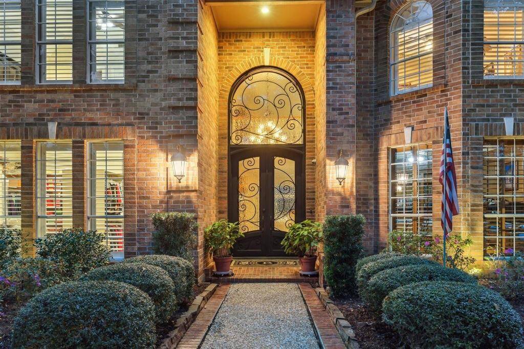 An ornate iron and glass double-door entry welcomes you with charm and sophistication. Framed by warm brick, elegant lighting, and lush garden beds, this is where curb appeal meets character.