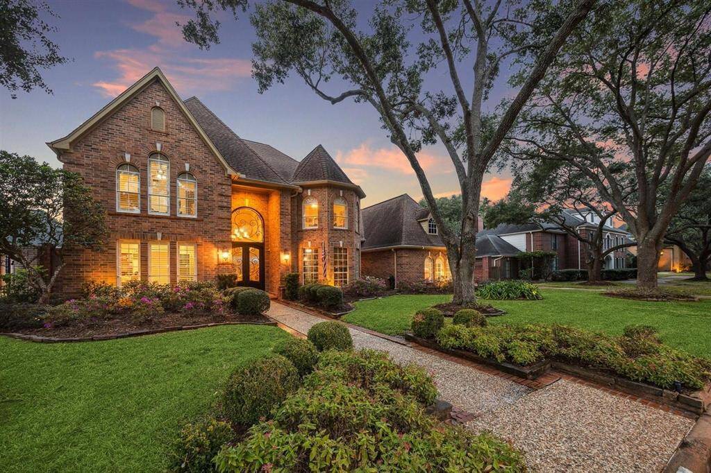 A storybook setting that instantly captivates! This side-angled twilight view reveals the home’s stately brick design, turret-style bay windows, and beautifully lit entryway. Surrounded by lush garden beds and framed by towering oaks, the walkway leads you to a place of warmth and elegance. From every angle, this residence exudes charm, comfort, and classic suburban luxury.