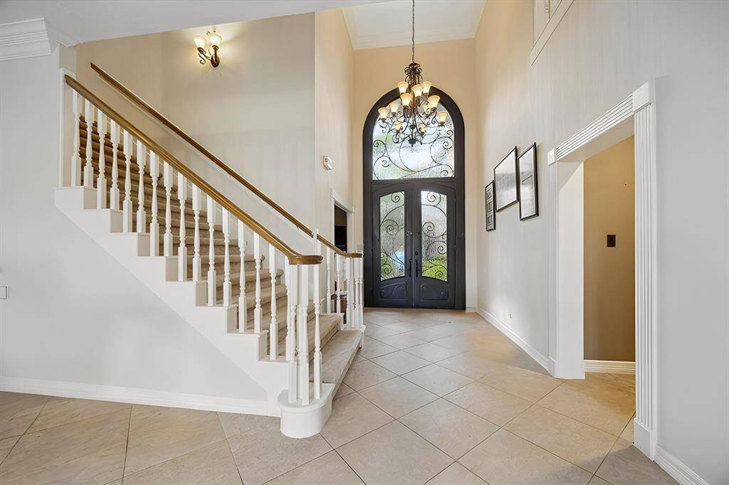 A soaring two-story foyer makes a grand first impression with its sweeping staircase, chandelier, and graceful sightlines. The wrought-iron double doors glow with natural light, setting a luxurious tone.