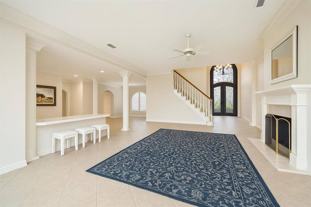 This light-filled living room impresses with architectural columns, a fireplace with mantle, and an open layout perfect for both everyday living and special gatherings. The bar seating adds a fun, functional touch.