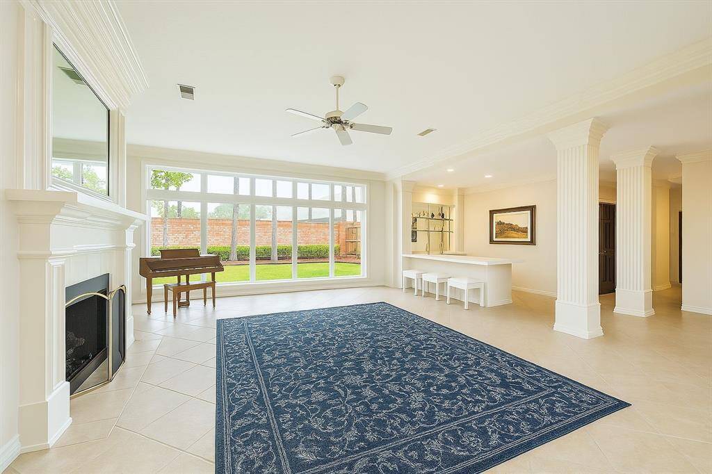 Walls of windows let natural light pour into this inviting living space, offering views of the manicured backyard. A fireplace, breakfast bar, and classic columns make it ideal for relaxing or entertaining.