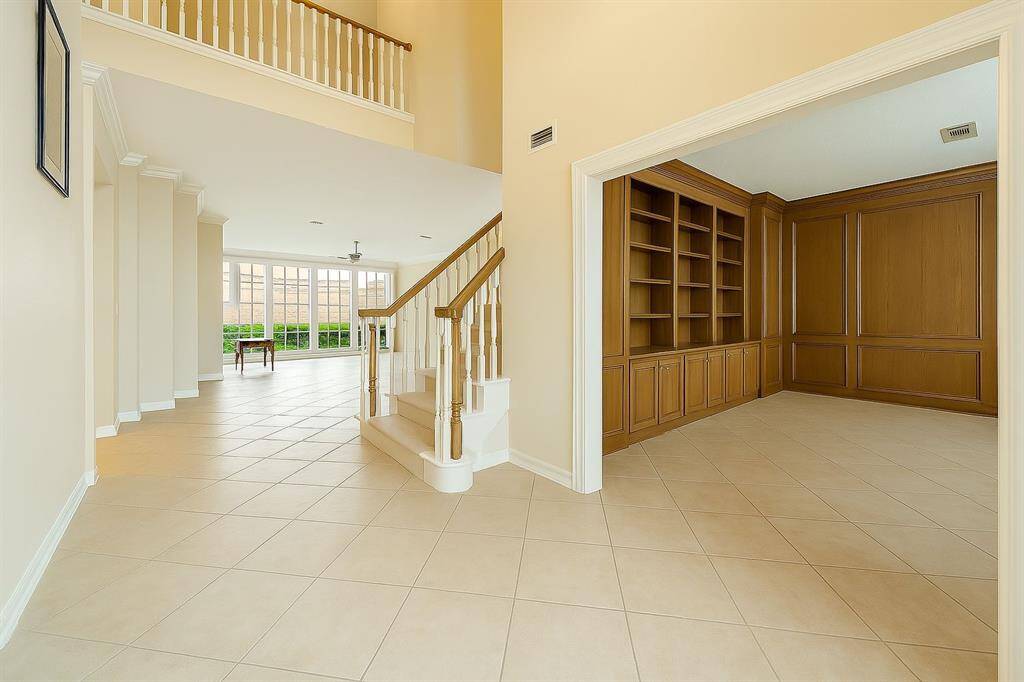 Step into a grand entryway featuring soaring ceilings, sweeping tile floors, and a view straight into the heart of the home. To your right, a sophisticated wood-paneled study with built-in cabinetry offers the perfect space for a home office or library.