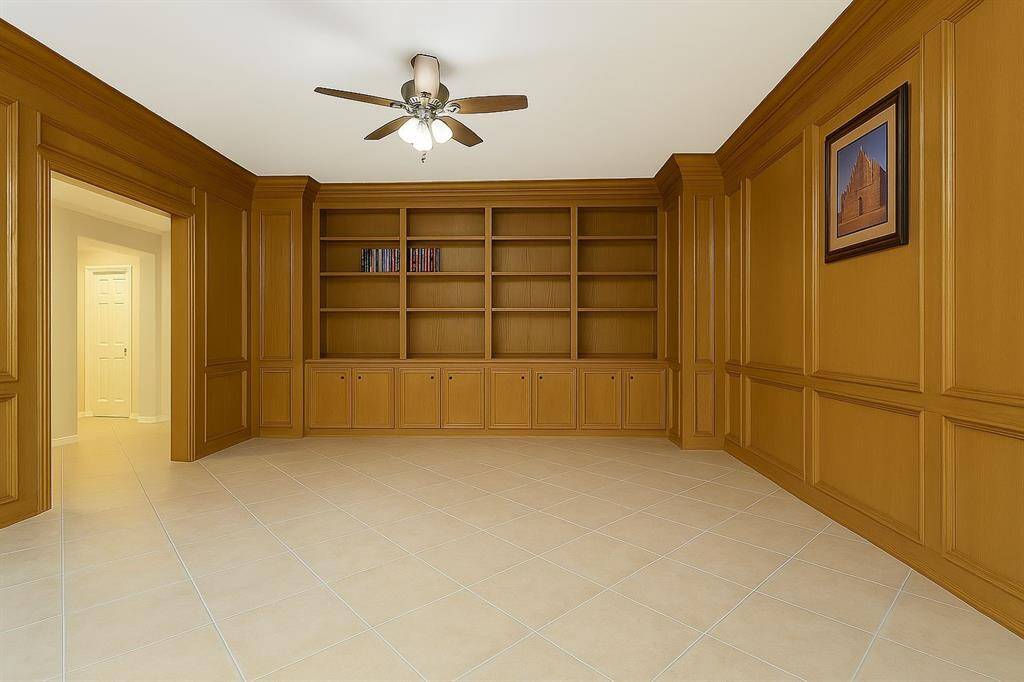 Classic elegance defines this rich, wood-paneled study. Wall-to-wall built-ins offer stylish storage and display, while the ceiling fan and lighting keep it bright and functional. A quiet retreat for working or reading.