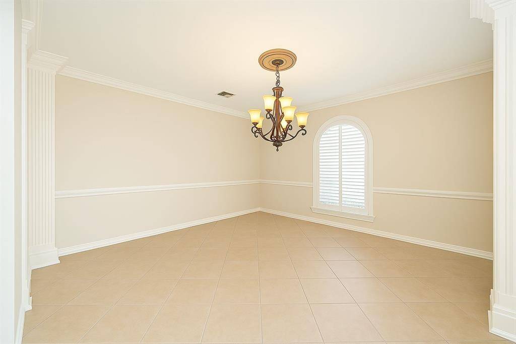 The formal dining room is timeless and sophisticated, with crisp white wainscoting, a classic chandelier, and a tall arched window dressed in shutters—perfect for hosting dinners in style.