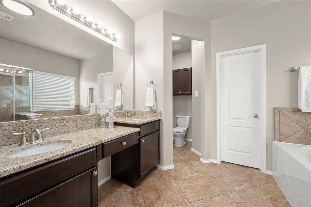 Primary ensuite boasts a neutral color pallet, granite tops, satin chrome fixtures, large tub and a seated vanity space.