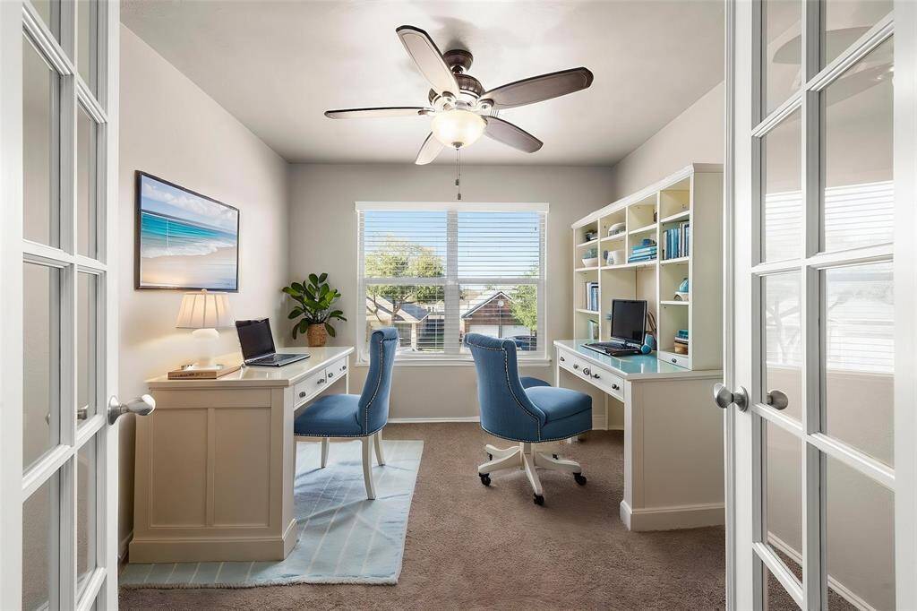 Home office with french doors, carpet, ceiling fan and a great view with large windows to keep you alert and in work mode.