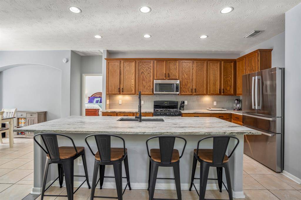 This chef-inspired kitchen features luxurious leathered granite counters, a massive island with an eating bar, and a deep single-basin undermount sink with a sleek pull-down faucet. Stainless steel appliances and tall upper cabinets offer both style and ample storage.