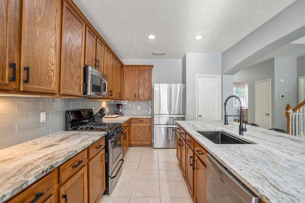 From the breakfast area, this view highlights the kitchen’s gorgeous leathered granite counters, stainless appliances, tall upper cabinets, and under-cabinet lighting. Straight ahead is the refrigerator with the pantry just beside it. To the right, you’ll spot the formal dining room through the arched opening in the distance and a convenient hall closet for extra storage.