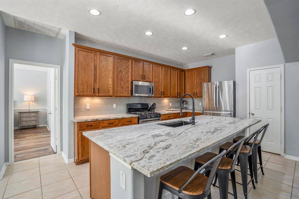One last look at the kitchen from under the grand archway into the living room highlights its thoughtful design—leathered granite counters, under-cabinet lighting, and stainless appliances offer both style and function. The oversized island with single-basin sink and pull-down faucet adds versatility, while the open layout keeps you connected to the living space beyond.