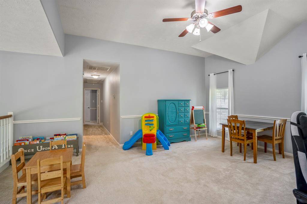 The upstairs loft-style game room offers a spacious and versatile retreat, highlighted by unique ceiling architecture with vaulted and pop-up details. Chair railing adds a polished touch, while abundant natural light makes this the perfect spot for relaxing or entertaining.
