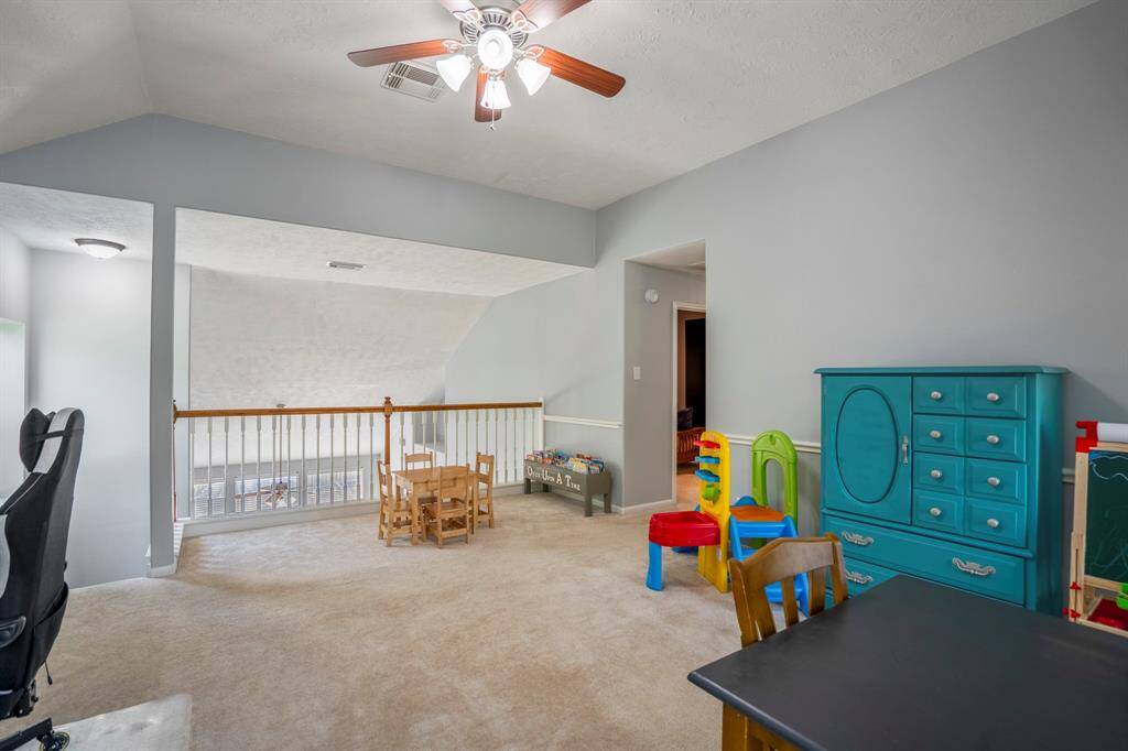 From this angle, we get a broader view of the spacious game room, showcasing the vaulted ceilings and natural light flooding in from the windows. The open feel is enhanced by the view towards the staircase, balcony railing, and the hallway leading to the media room, emphasizing the expansive layout of this flexible space.