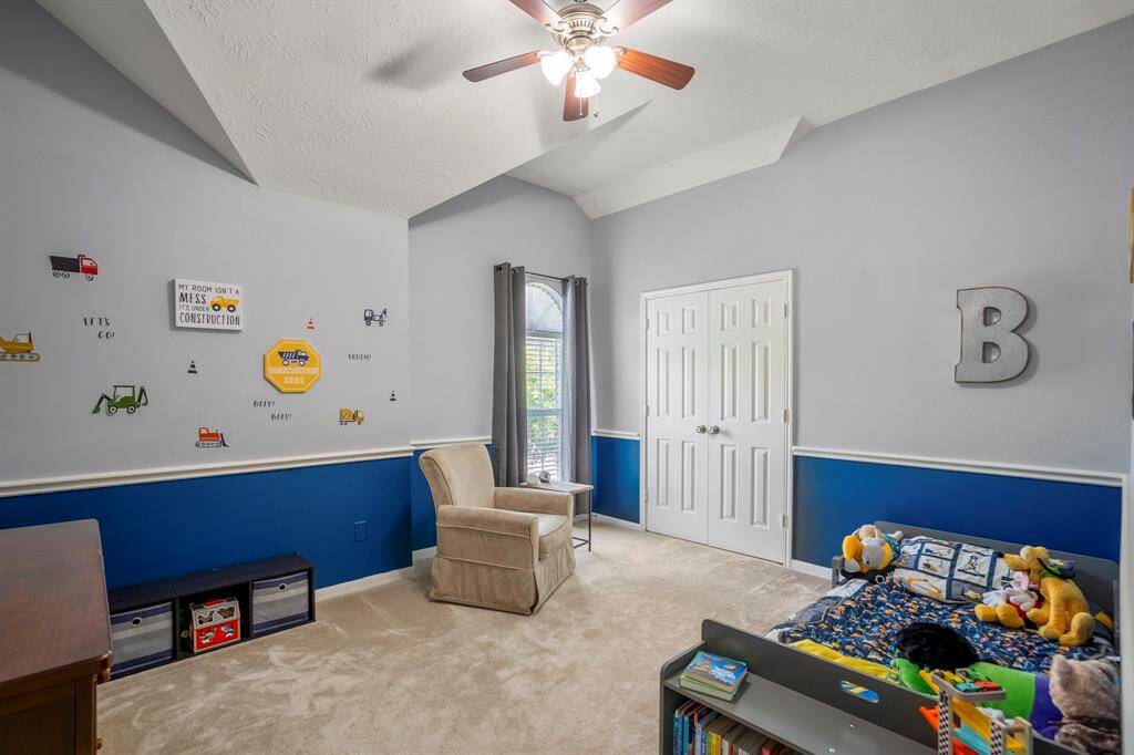 This charming upstairs bedroom features a vaulted ceiling with unique architectural details, adding character and depth to the space. The elegant chair railing complements the design, while double doors open to a spacious closet, offering plenty of storage.